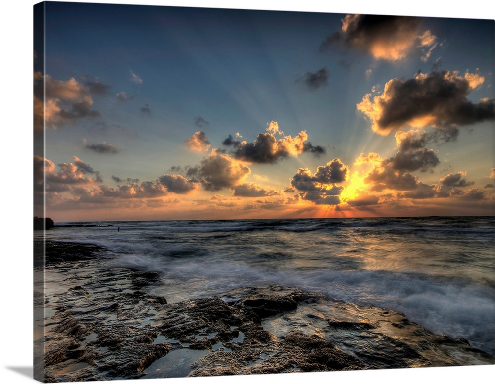 Horizontal photograph of a vibrant, golden sunset at a rocky beach.