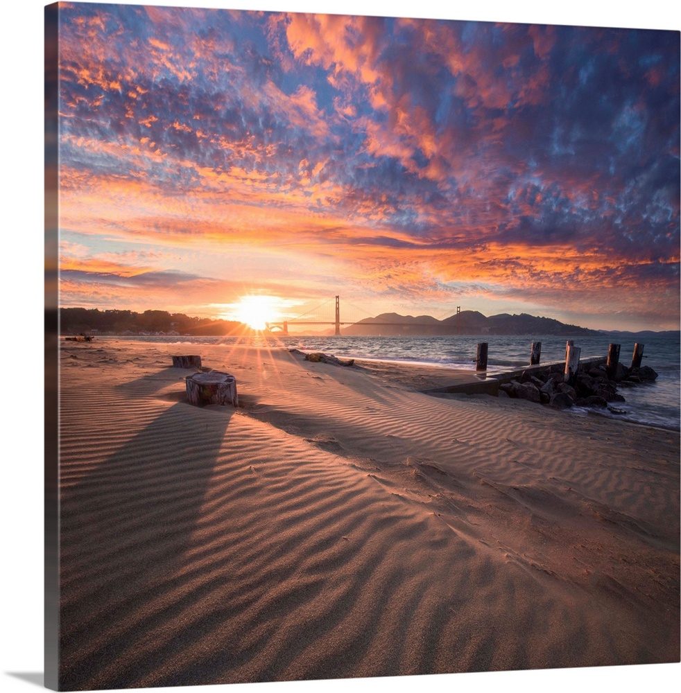 A square photograph of a beach with the golden gate bridge in the background at sunset.