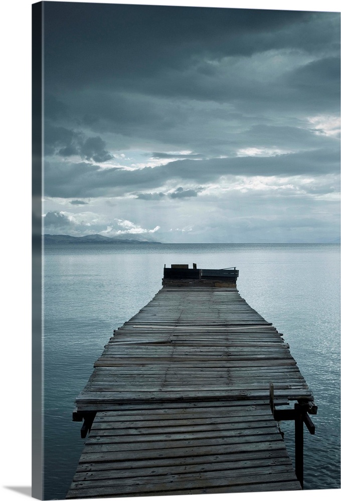 Photograph of a weathered dock over calm water with dark clouds overhead.