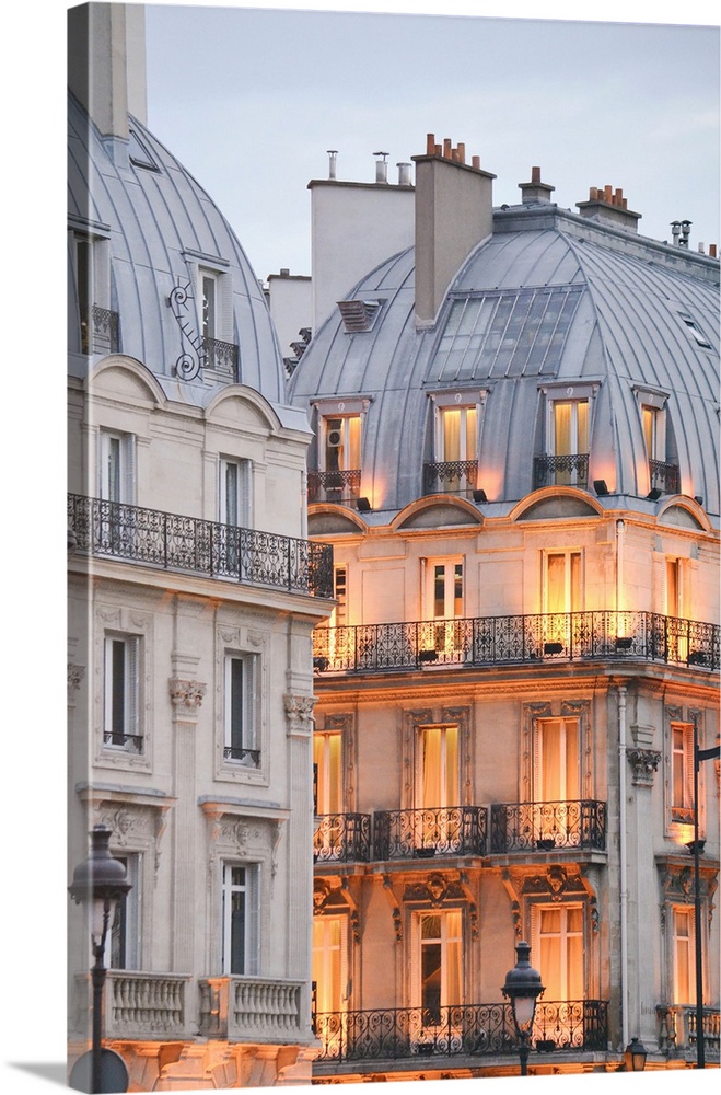 A photograph of Paris apartment buildings at dusk with lights beginning to warm the faade
