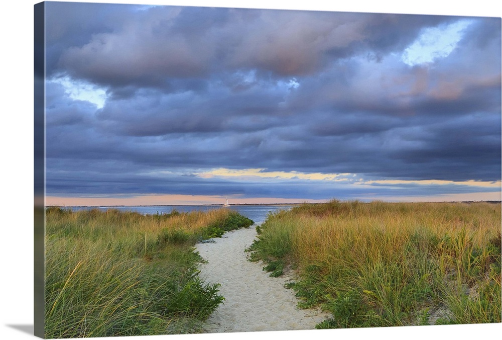 A photograph of a sandy pathway leading to an idyllic beach, with dark puffy clouds overhead.