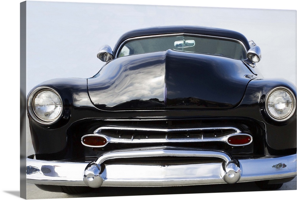 The front of a classic car with a chrome bumper and dark paint.