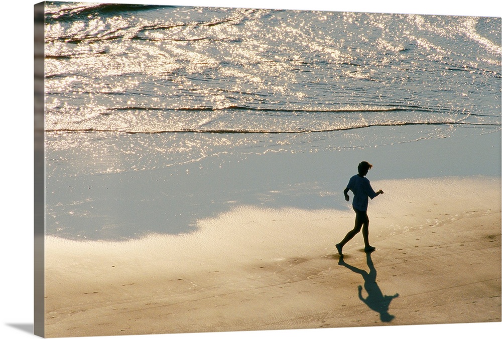 A jogger in silhouette runs on the surf line of the beach as the morning light begins to rise.