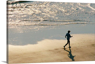 A jogger in silhouette runs on the surf line of the beach