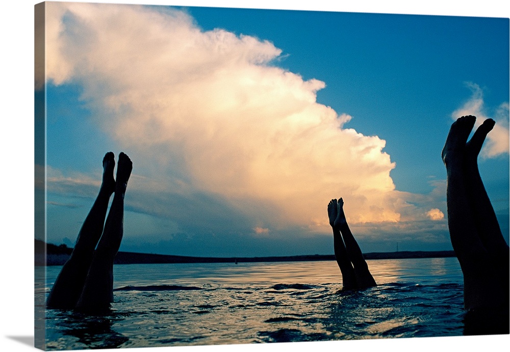 Three pairs of legs stick out of the water in Lake McConaughy, as a thunderstorm creeps forward in the distance.