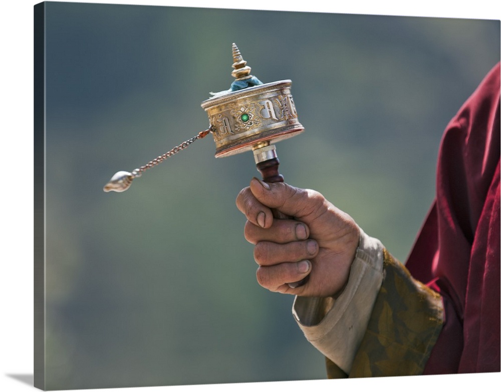 A Buddhist spins his hand-held prayer wheel in a clockwise direction with the help of a weighted chain attached to it. Eac...