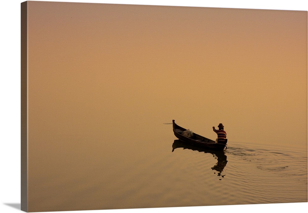 Myanmar, Burma, Amarapura. A fisherman paddling across Taungthaman Lake at sunrise, Amarapura.