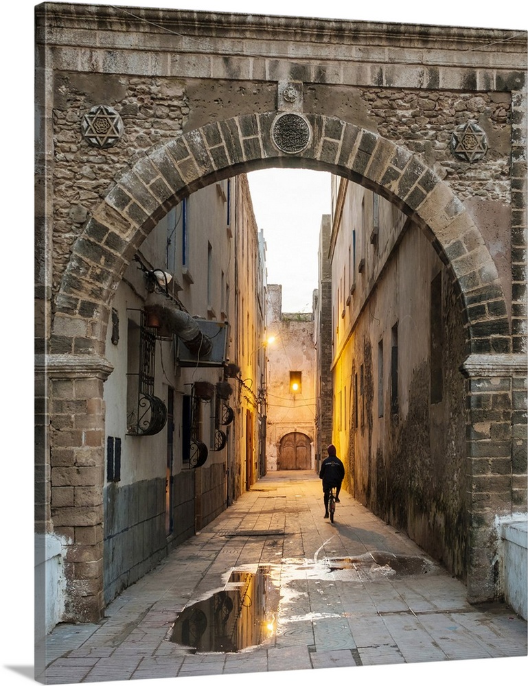 Morocco, Marrakesh-Safi (Marrakesh-Tensift-El Haouz) region, Essaouira. A person rides a bicycle through a dark alley in t...