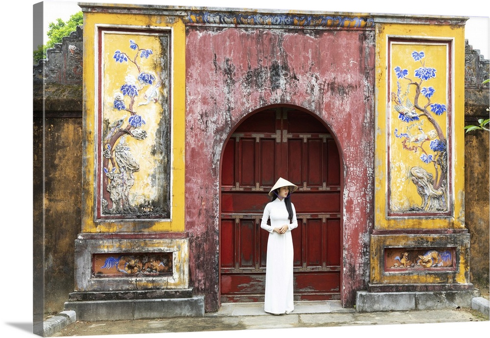 A Vietnamese girl in an Ao Dai dress stands in front of a historical gate in Hue Imperial Citadel, Hue, Thua Thien-Hue pro...