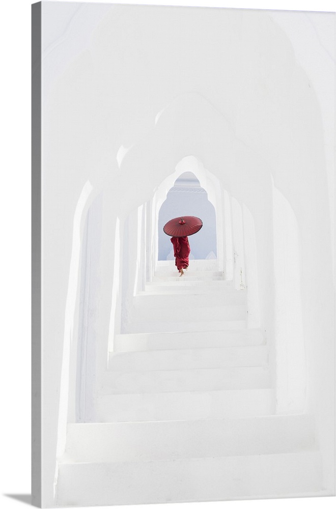 A young Buddhist monk holding a red umbrella walks up the steps in Hsinbyume Pagoda, Mingun, Mandalay, Myanmar.