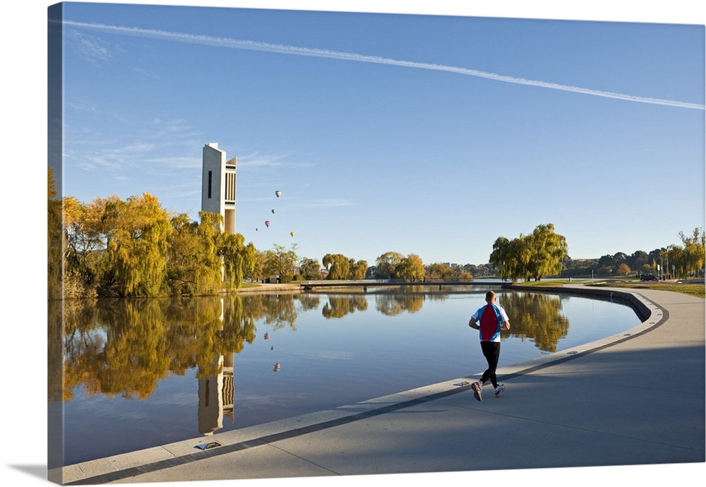 Australia, Australian Capital Territory (ACT), Canberra. Man jogging beside Lake Burley Griffin with the National Carillon...