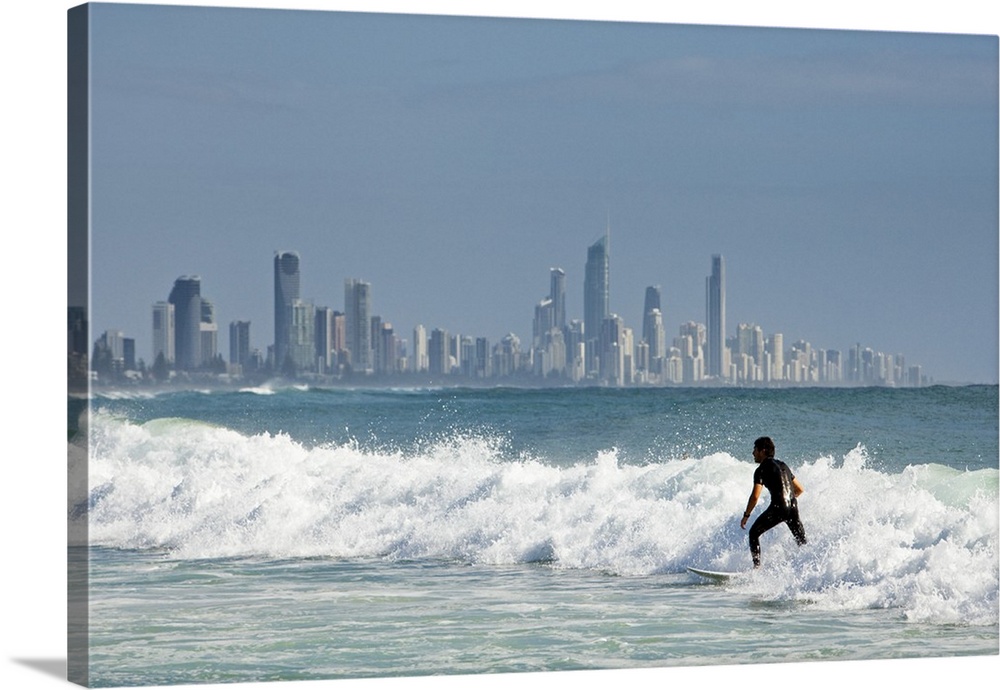 Australia, Queensland, Gold Coast, Burleigh Heads. Surfer riding waves with Surfers Paradise skyline in background.