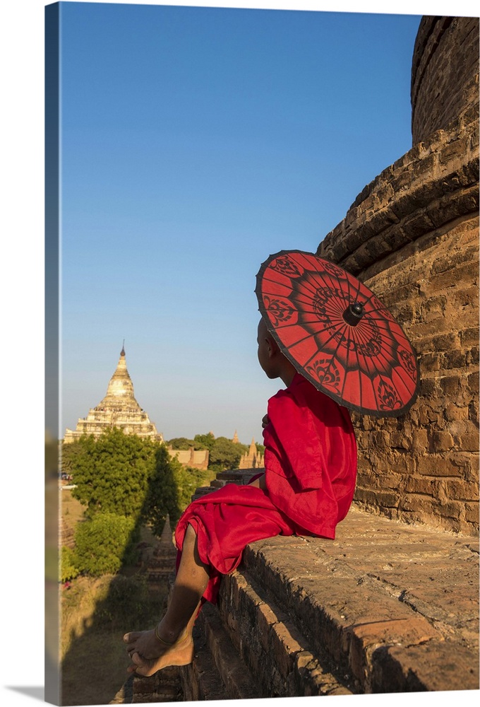 Bagan, Mandalay region, Myanmar (Burma). A young monk with red umbrella watching the Shwesandaw pagoda in a distance.