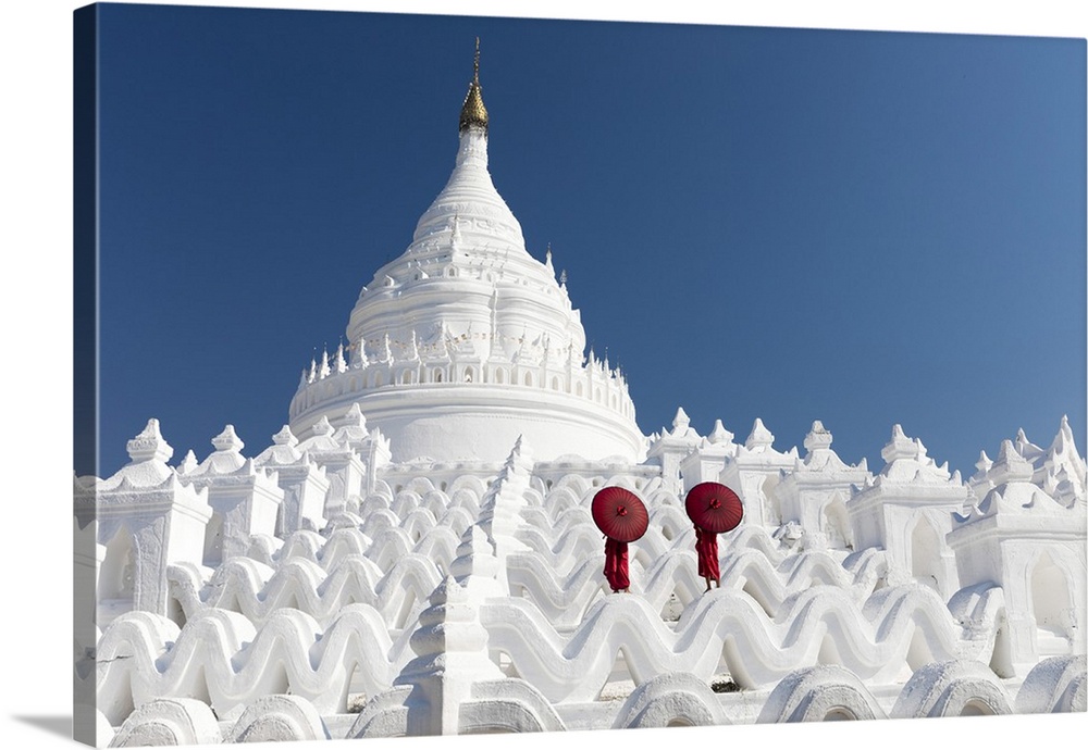 Two young Buddhist monks stand on the white walls of Hsinbyume Pagoda holding red umbrellas, Mingun, Mandalay, Myanmar.