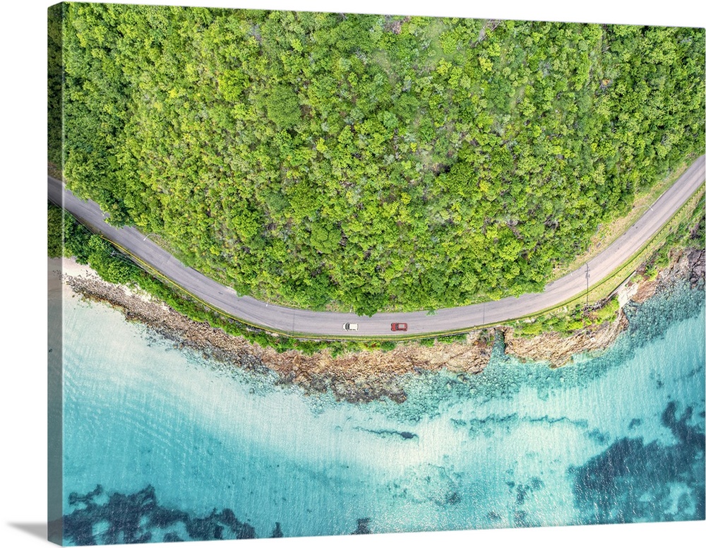 Cars traveling on a coastal road in between the crystal Caribbean sea and lush plants, aerial view, Antigua, Antigua & Bar...