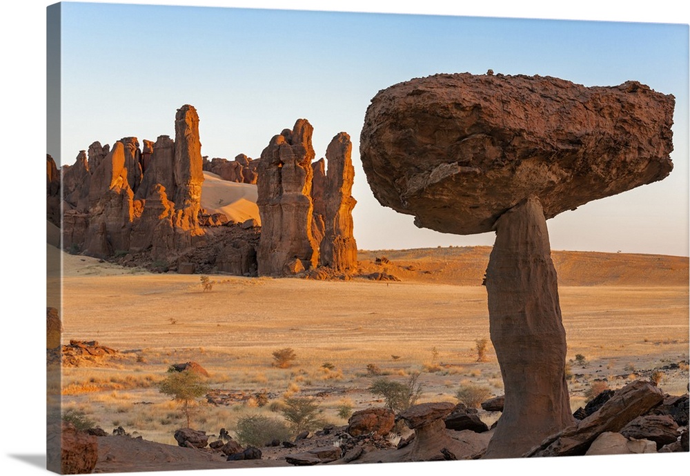 Chad, Chigeou, Ennedi, Sahara. Weathered red sandstone in a desert landscape with a large mushroom-like feature of balanci...