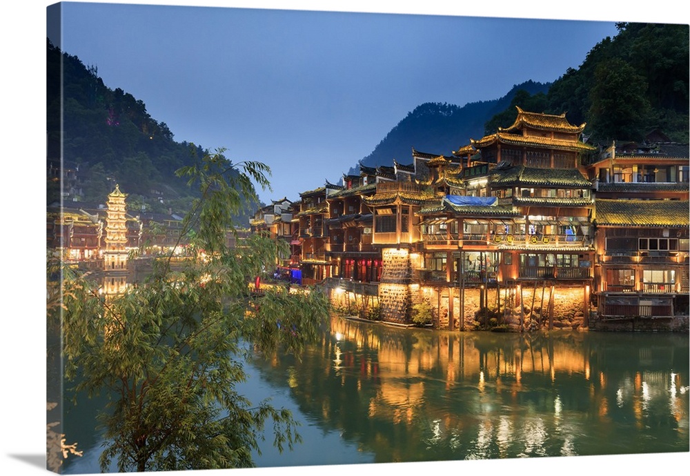 China, Hunan province, Fenghuang, riverside houses by night reflecting in the river.