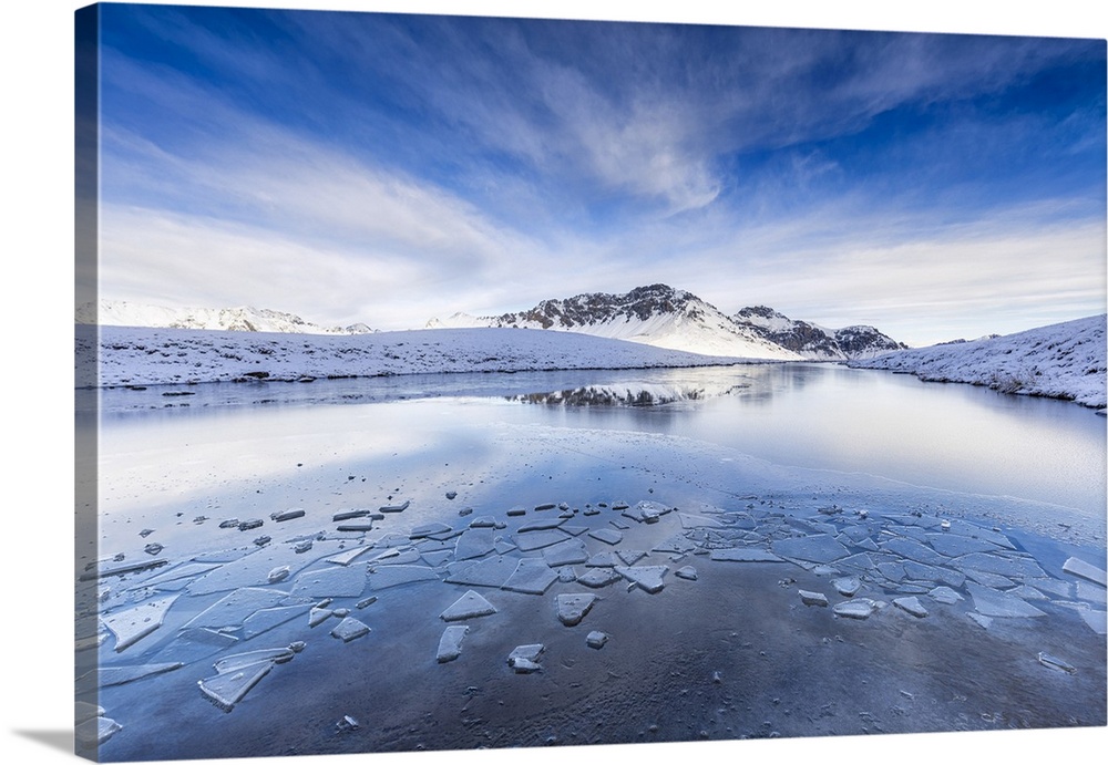 Clouds is reflected in the icy surface of alpine lake. Stelvio pass, Valtellina, Lombardy, Italy