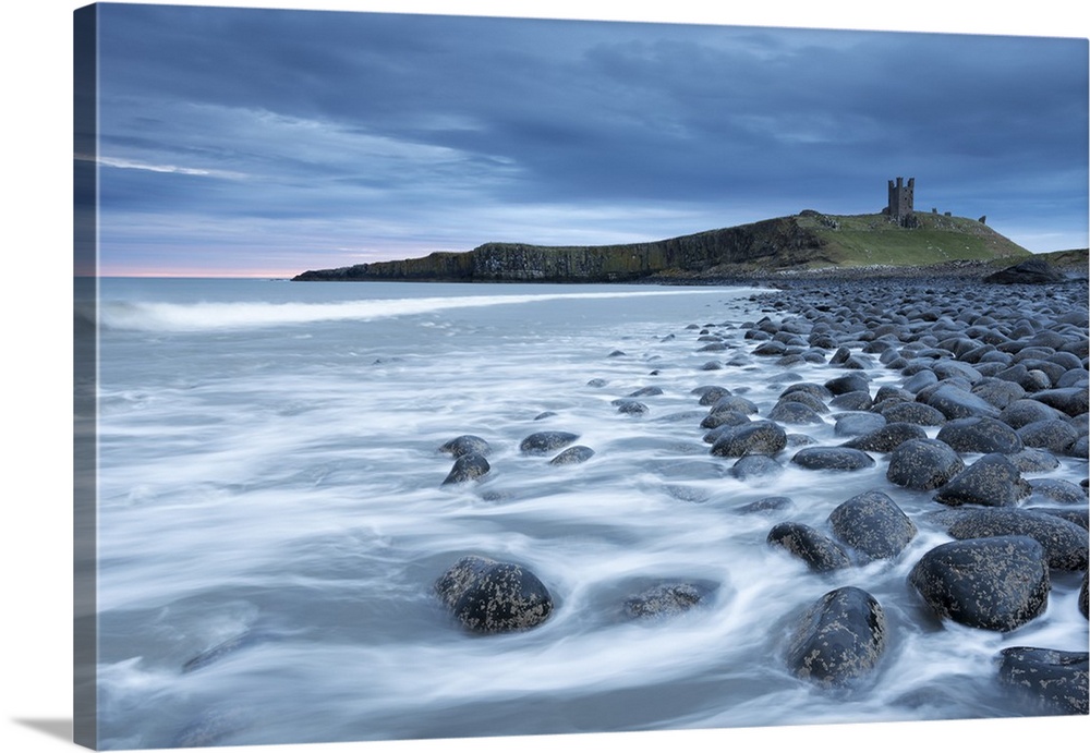 The ruins of Dunstanburgh Castle overlooking the boulder strewn shores of Embleton Bay, Northumberland, England. Spring (A...