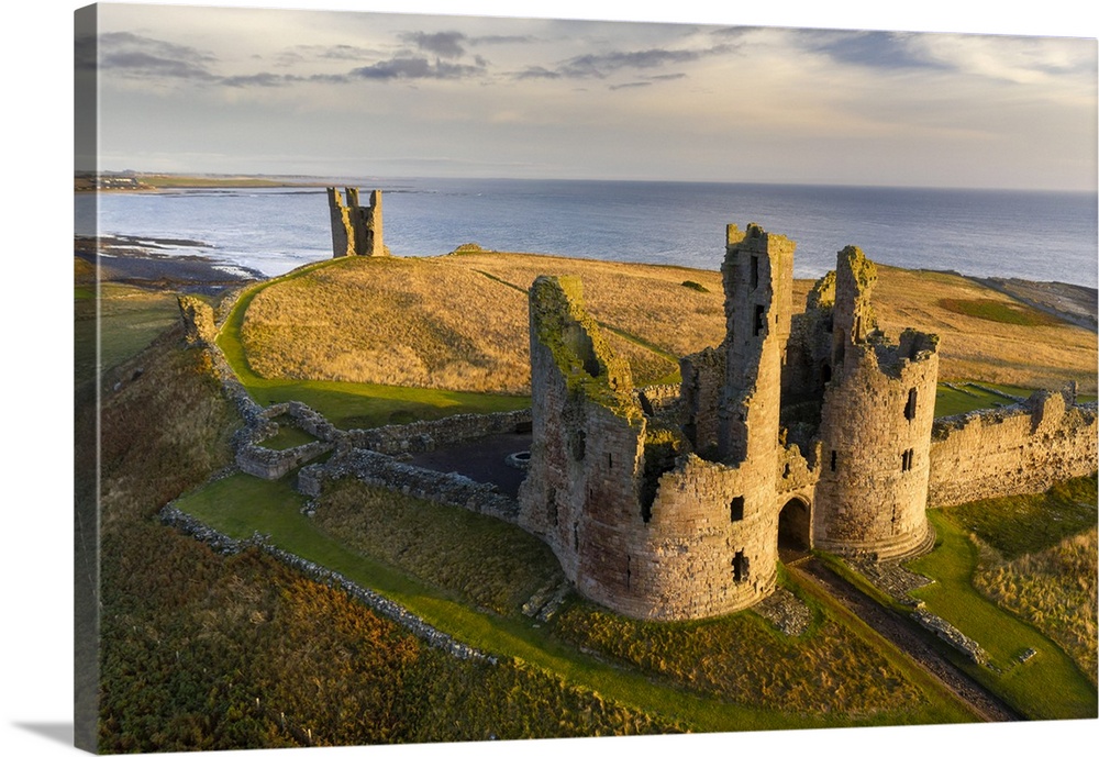 Dunstanburgh Castle's great gatehouse and Lilburn Tower illuminated in early morning sunlight, Northumberland, England. Au...