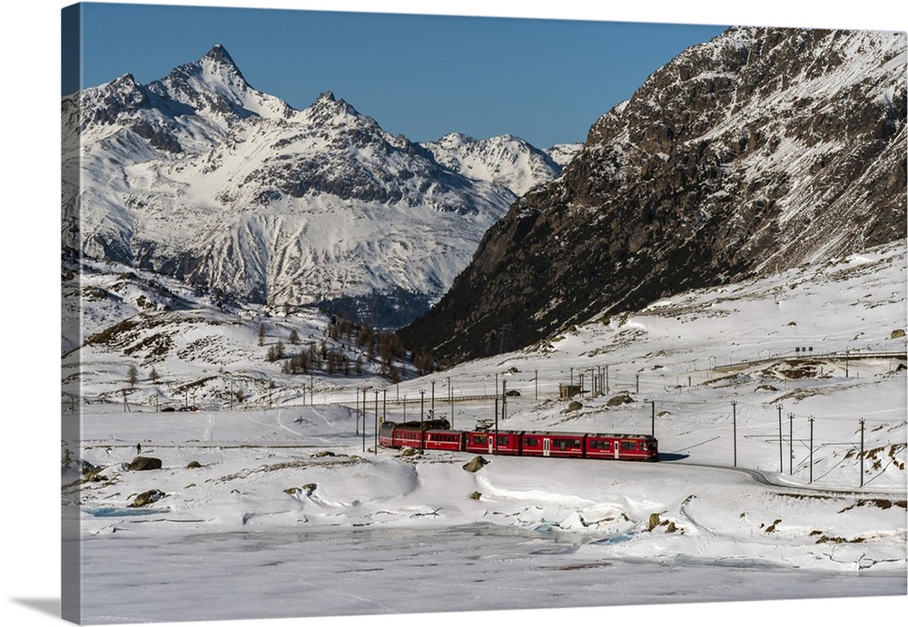 The famous Bernina Express red train passing Lago Bianco in a scenic winter mountain landscape, Graubunden, Switzerland