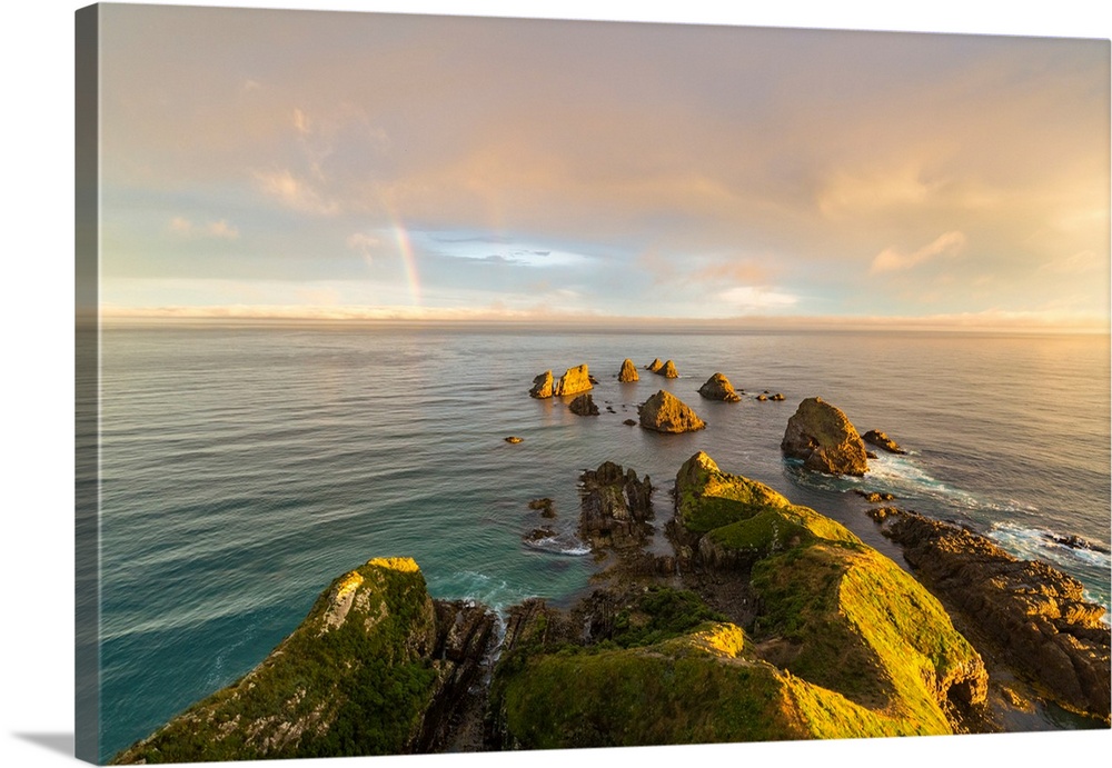 Golden light on The Nuggets islands and rainbow in the sky at Nugget Point. Ahuriri Flat, Clutha district, Otago region, S...