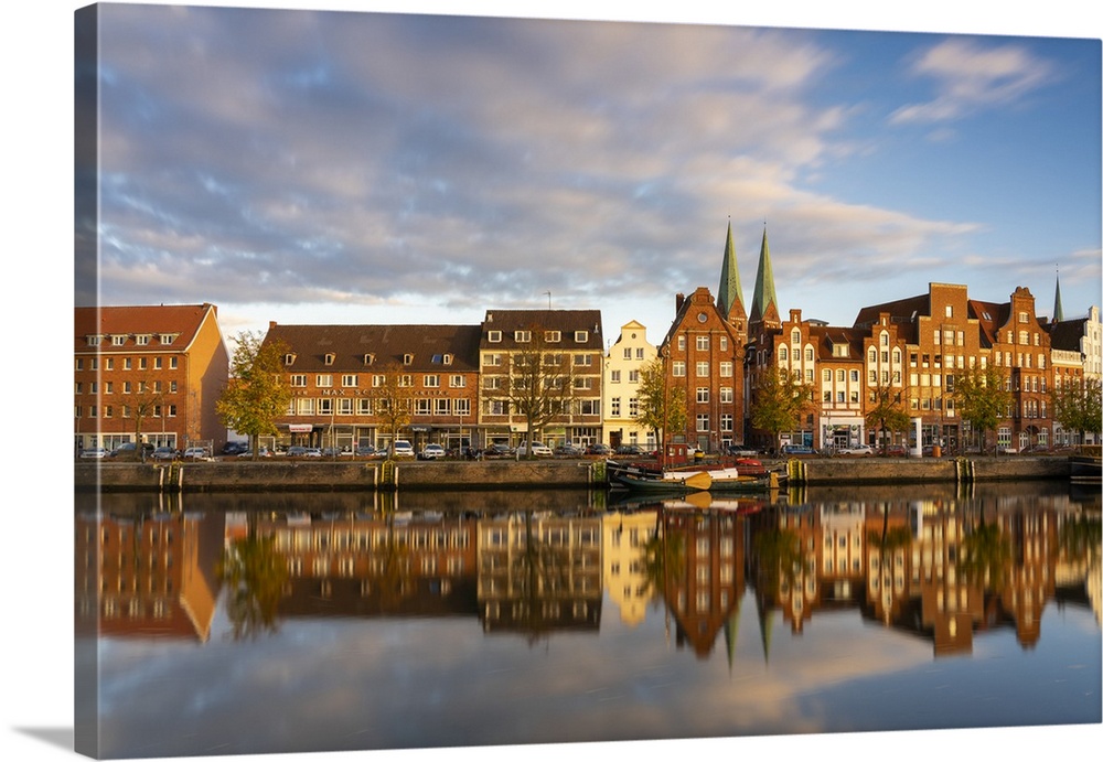 Houses on riverfront of Trave river with towers of St. Marienkirche church in background at sunset, Lubeck, UNESCO, Schles...