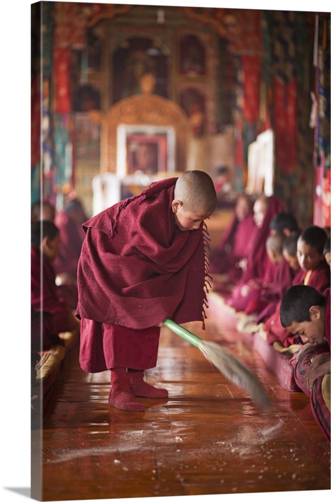 India, Ladakh, Thiksey. Young novice monk sweeping up the tsampa crumbs at morning prayers or puja, Thiksey Monastery.