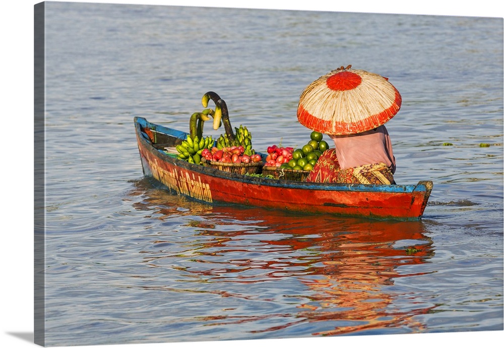 Indonesia, South Kalimatan, Lok Baintan. A market vendor in a wide-brimmed hat rows her small fruit-laden wooden boat to a...