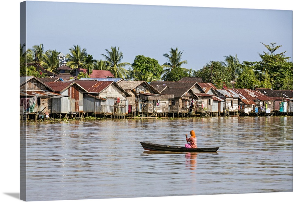 Indonesia, South Kalimatan, Banjarmasin. A woman rows towards houses on stilts lining the banks of the Barito River. Appro...