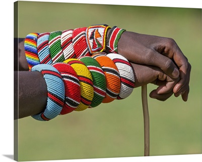 Kenya, A Samburu warrior with beaded bracelets rests his hands on a walking stick