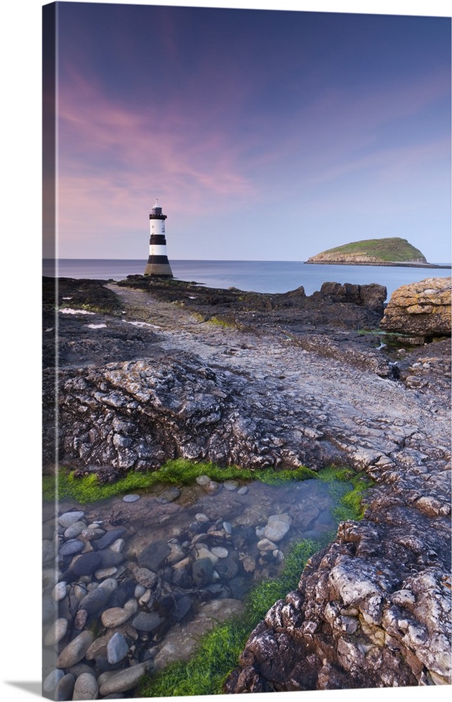 Twilight on the rocky Anglesey coast looking towards Penmon Point Lighthouse and Puffin Island, Anglesey, North Wales, UK....
