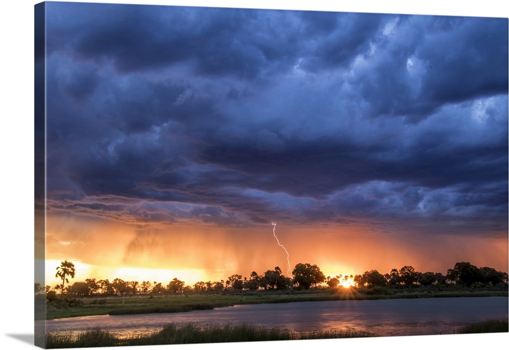 Lightning shoots from a summer thunderstorm as the sun sets behind it, Okavango Delta, Botswana