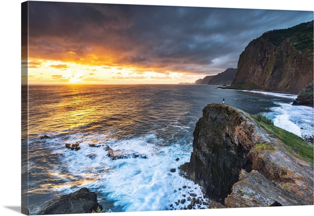 Man on cliffs looking at waves at dawn, Miradouro Do Guindaste viewpoint, Madeira island, Portugal.