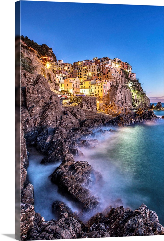 Manarola village illuminated by the blue light of dusk with its typical pastel colored houses. Cinque Terre National Park....