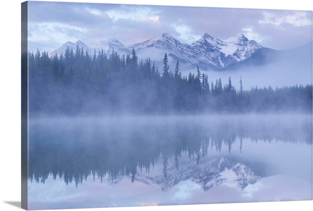 Snow capped mountains reflect in a misty Herbert Lake, Canadian Rockies, Banff National Park, Alberta, Canada. Autumn, Sep...