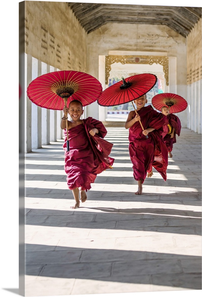 Myanmar, Mandalay division, Bagan. Three novice monks running with red umbrellas in a walkway (MR)