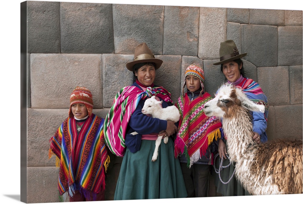 South America, Peru, Cusco. Quechua people standing in front of an Inca wall, holding a lamb and a llama and wearing tradi...