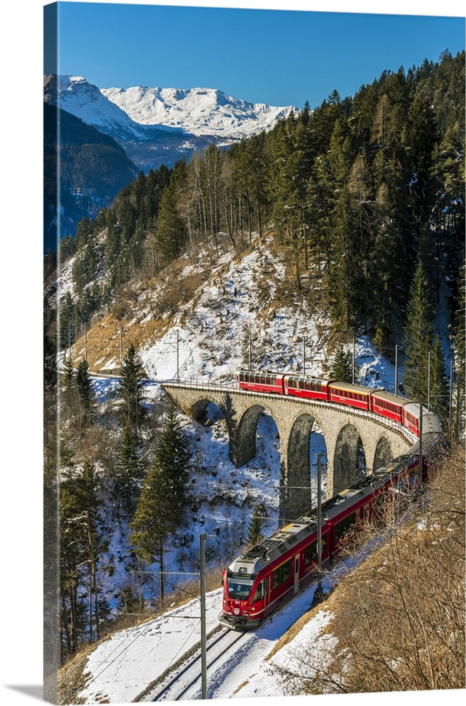 The famous red train of Albula mountain railway passing through a scenic winter alpine landscape near Filisur, Graubunden,...