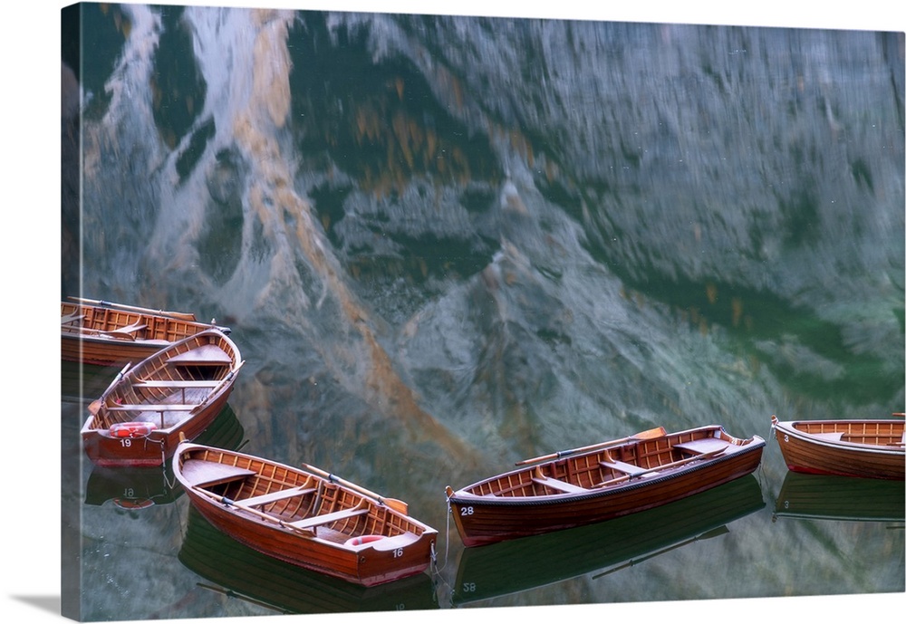 Row boats floating in the Braies lake on a calm morning, with the mountains reflecting in the water. Dolomites, Italy.