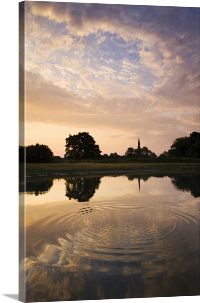 Salisbury Cathedral Spire and a beautiful dawn sky reflected in a rippled pond, Salisbury, Wiltshire, England. Summer, Jun...