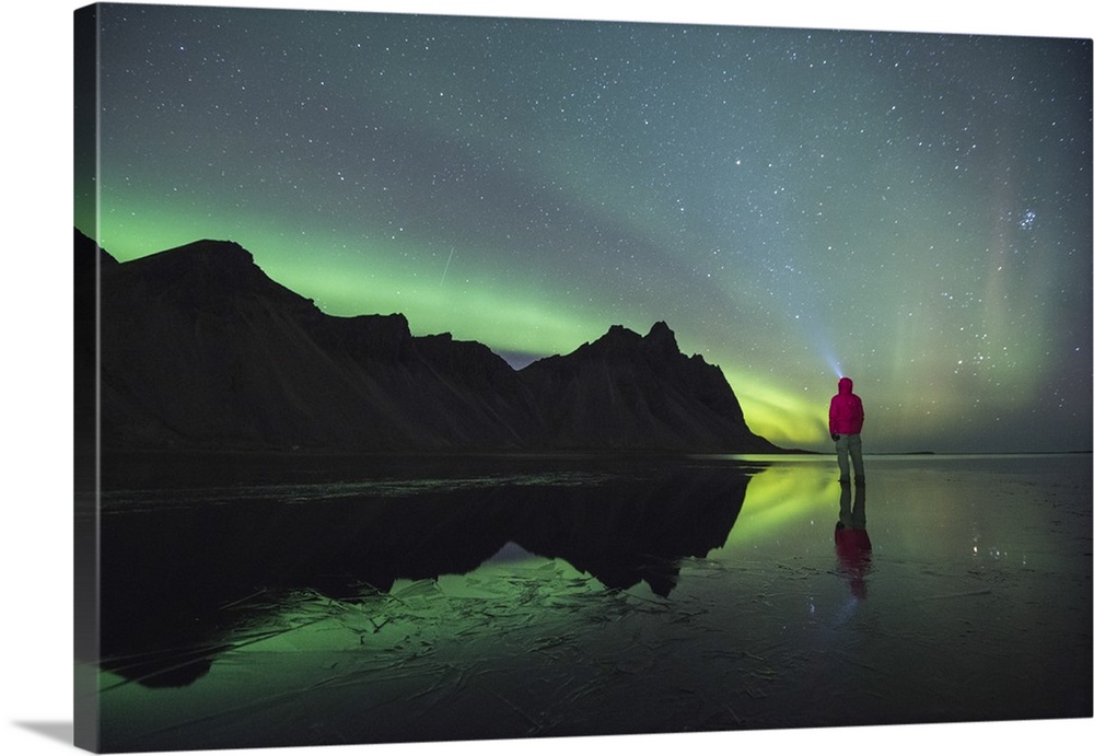 Stokksnes, Hofn, Eastern Iceland, Northern Europe. One man standing on the beach at night gazing at the northern lights an...
