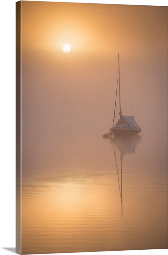 Sun rising over a sailing boat moored on a misty Wimbleball Lake, Exmoor National Park, Somerset, Engtland. Spring (May) 2...
