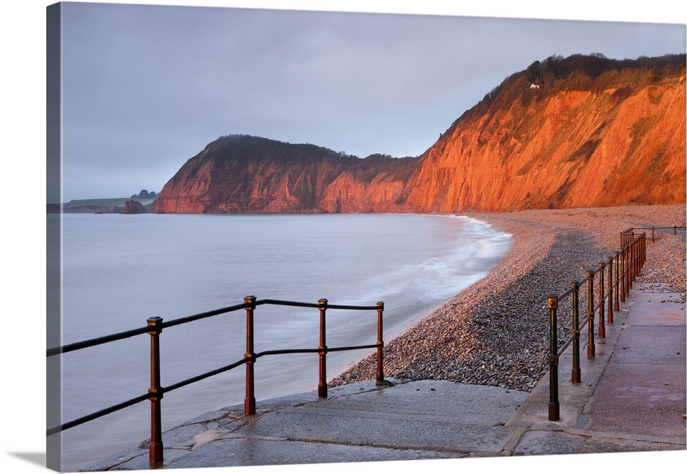 Early morning sunlight glows against the distinctive red cliffs of High Peak, viewed from the beach at Sidmouth, Devon, En...
