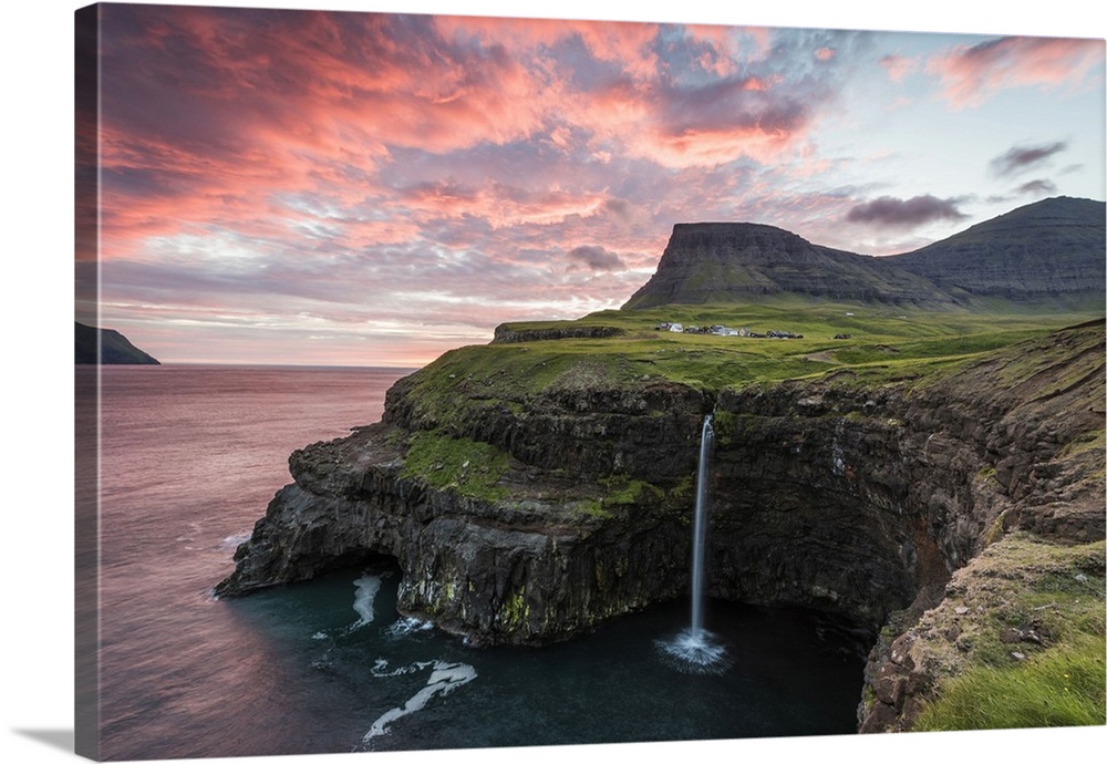 Gasadalur, Vagar island, Faroe Islands, Denmark. The iconic waterfall jumping from the cliff into the ocean at sunset.
