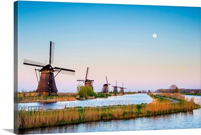 The moon rises above historic Dutch windmills on the polders at sunset, South Holland