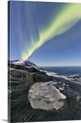 The Northern Lights illuminates the rocky peaks and icy sea in the polar night