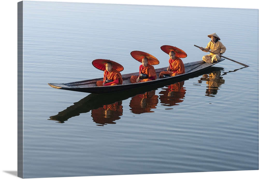 Three monks in orange robes with bowls for alms giving and a leg-rowing fisherman commute using a boat across Lake Inle, N...