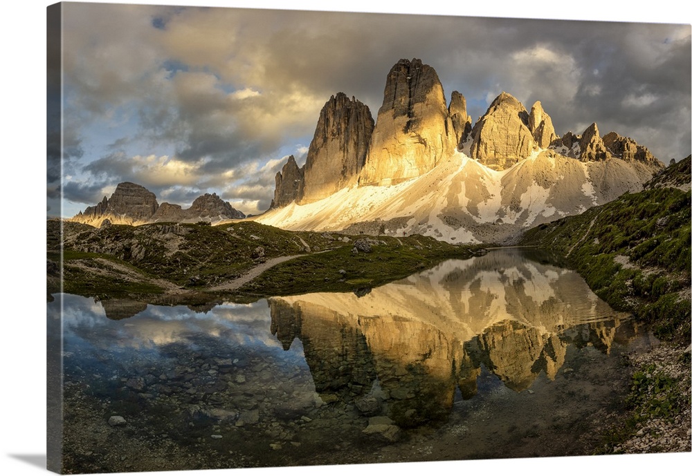 Tre Cime di Lavaredo are reflected in an alpine lake during a sunset with warm light, Dolomiti, Unesco World Heritage Site...