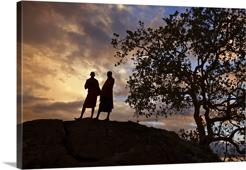 Two Maasai men silhouetted on a hill at sunset.